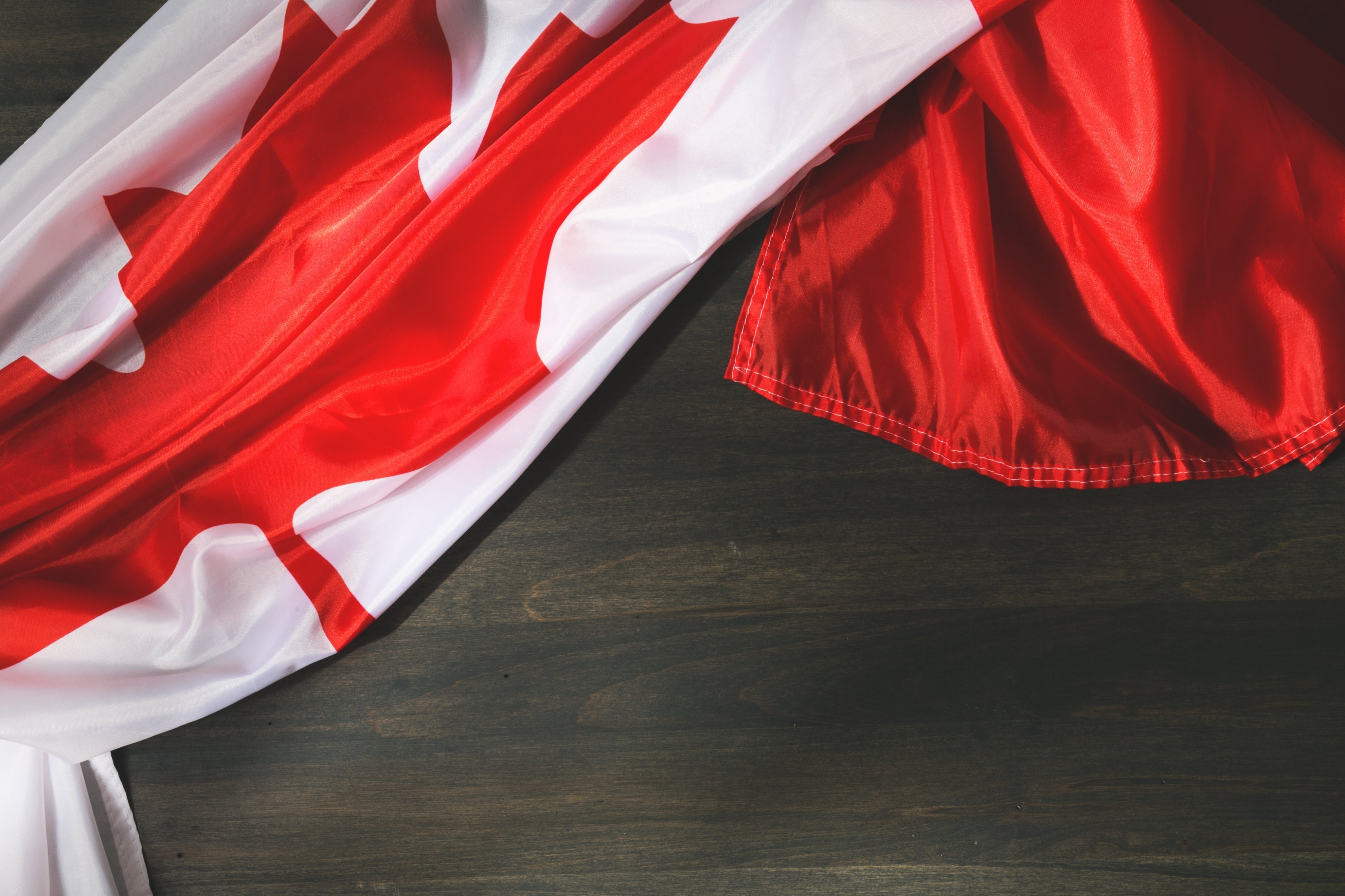 A folded Canadian flag draped over a dark wood grain surface.