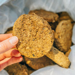 Close-up of a hand holding a single Hypoallergenic freeze-dried dog food puck, with more pucks visible in the bag below.