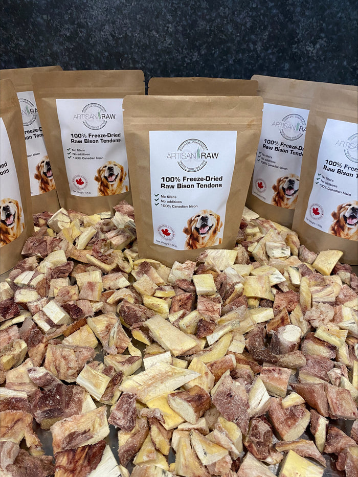 Several Artisan Raw Bison Tendons treat bags arranged upright on a bed of dried bison tendon pieces.